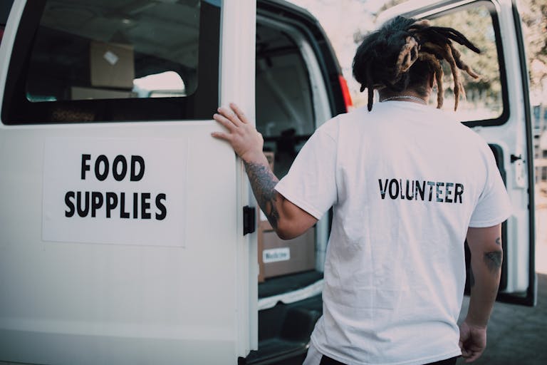 Volunteer unloading a van labeled "Food Supplies" — representing real-world nonprofit auto insurance needs for organizations using vehicles in community service.